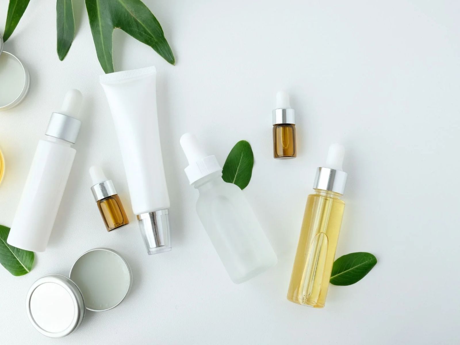 Flat lay of serum bottles and creams with green leaves