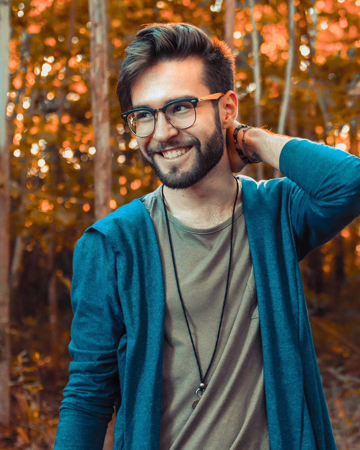 Smiling man in glasses and a teal cardigan in front of autumn trees