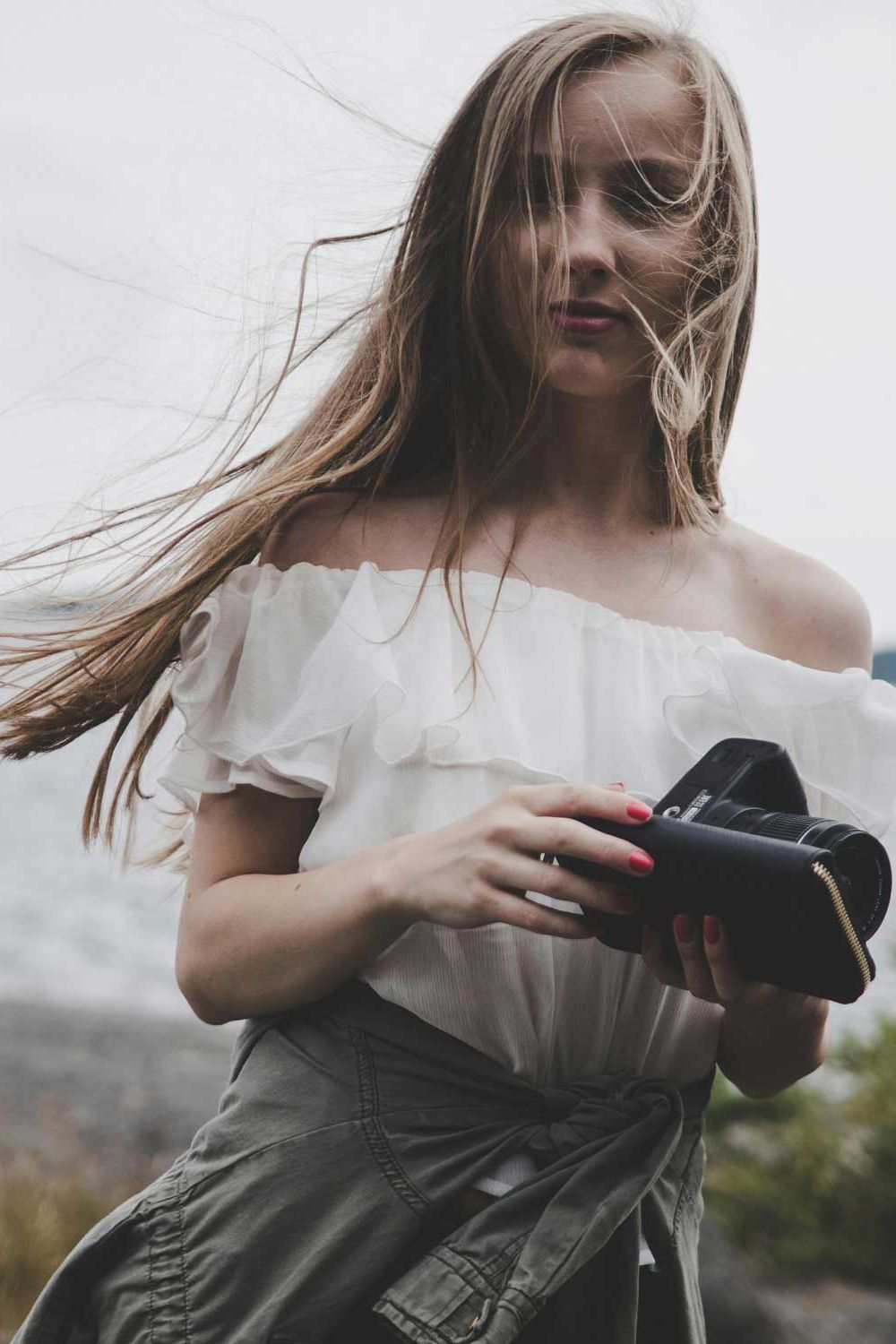 Woman holding a film camera on a windy coast, hair blowing